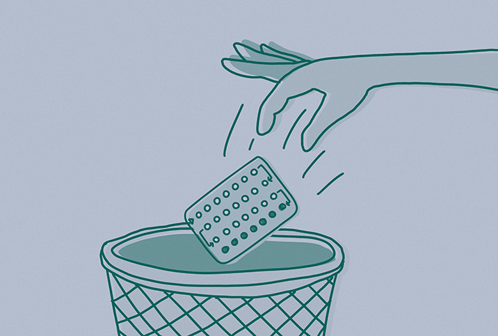 A hand throws away a packet of pills into a waste bin.