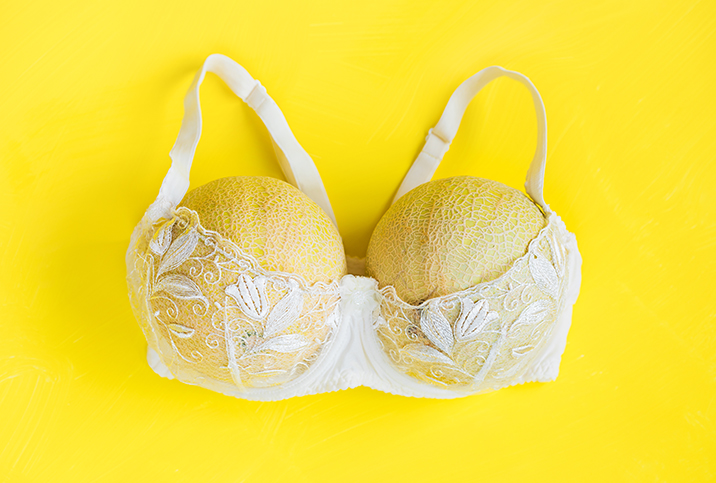 Two honeydew melons fill out a white, lacy bra on a yellow background.