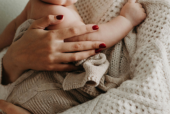 A woman in a knitted sweater holds a baby in her arms.