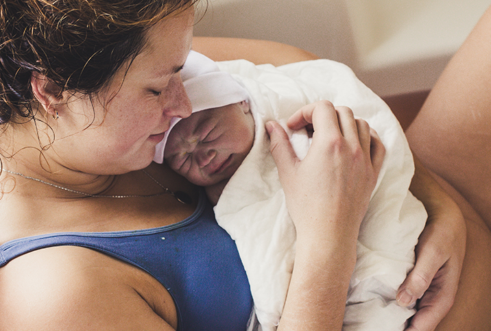 A woman holds her newborn baby after unassisted birth.