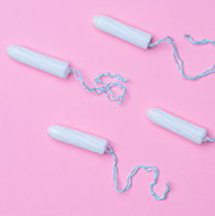 Four tampons without applicators lay against a pink surface.