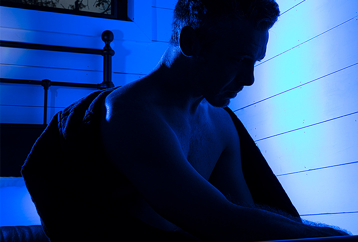 A shadowy figure sits in bed with a blue light shining behind.