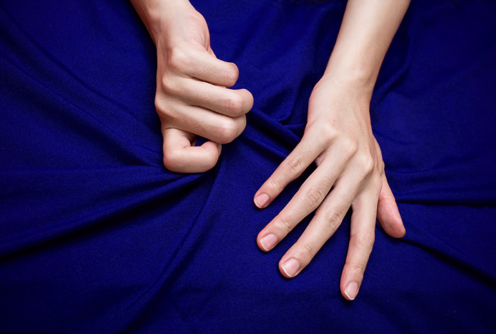 One hand grips a blue sheet next to another more relaxed hand.
