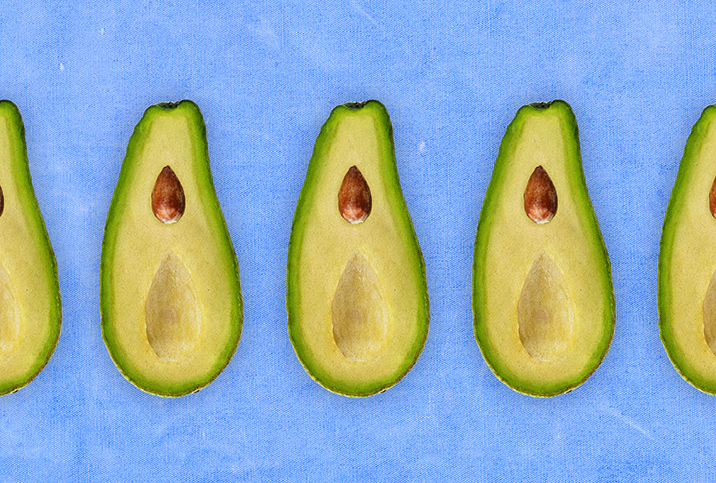 A row of avocados cut in half is against a blue background.