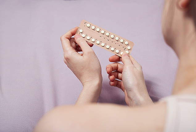 A woman holds up a packet of birth control pills.
