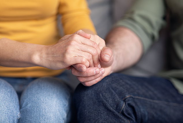 A close up photo of a couple holding hands along their touching knees.