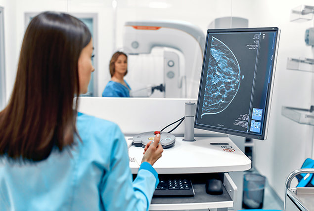 A technician looks over a screen showing an outline of a breast during a mammogram.