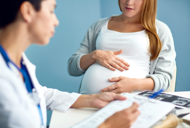 A woman holds her pregnant belly while sitting in front of a doctor.