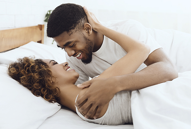 man and woman hold each other in bed with white sheets