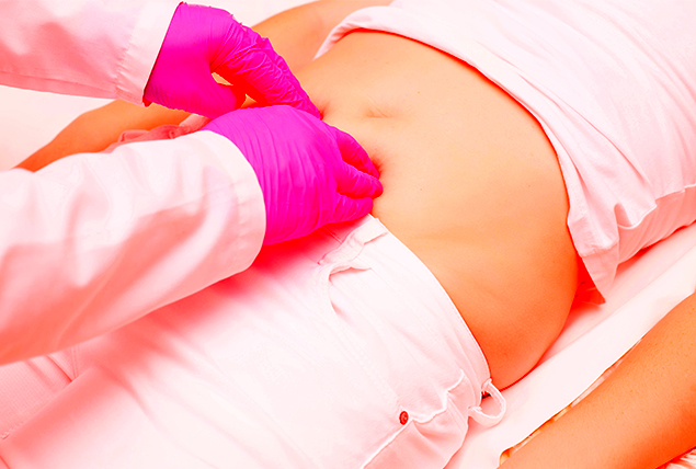pink gloved hands exam a woman stomach as she lays on a doctors table