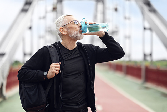 older man in active clothes drinks from blue water bottle white on a walk