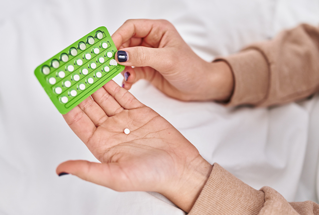 A pair of hands holds a green packet of white pills.