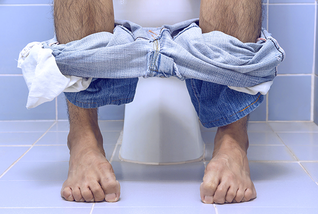 legs and feet sitting on toilet with pants down around ankles