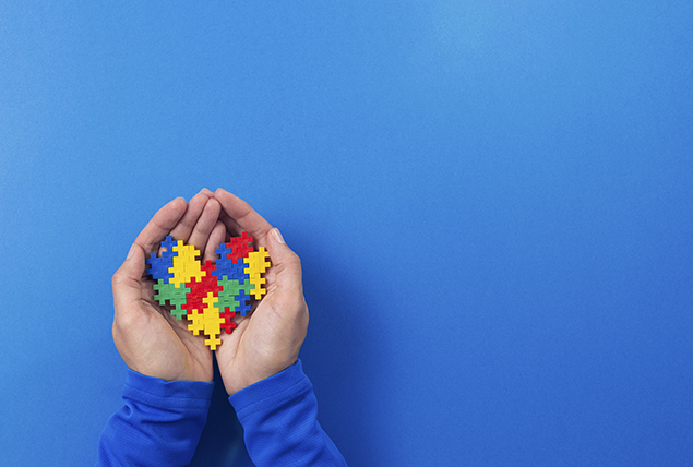 A pair of hands hold a multi-colored puzzle in the shape of a heart.