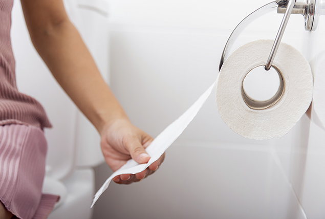 A woman pulls toilet paper from a roll while sitting on the toilet.