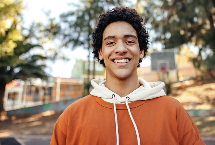 A-teenage-boy-stands-outside-and-smiles-at-the-camera