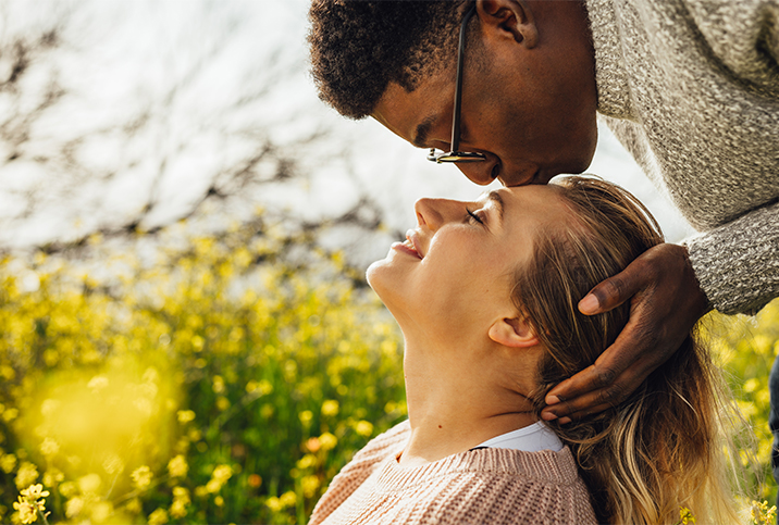 A man leans over a woman and kisses her forehead.