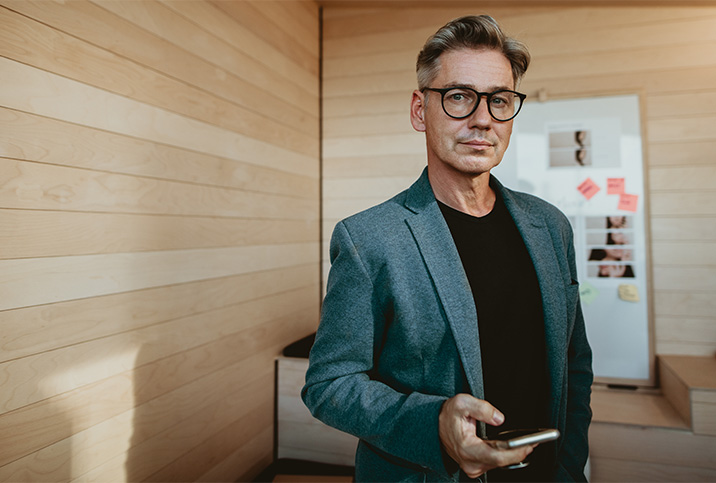 A man stands with his cellphone in hand looking at the camera.