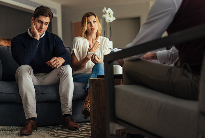 A man rubs his face while his partner talks to a licensed professional during couples therapy.