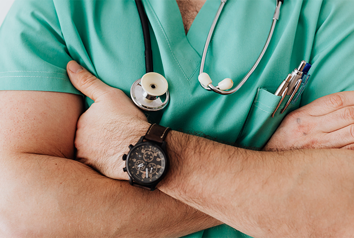 The upper body of a doctor is shown with his arms crossed against his chest.