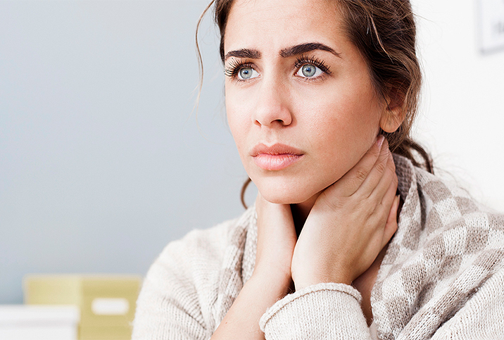 A woman rests her hands on her neck and looks concerned.