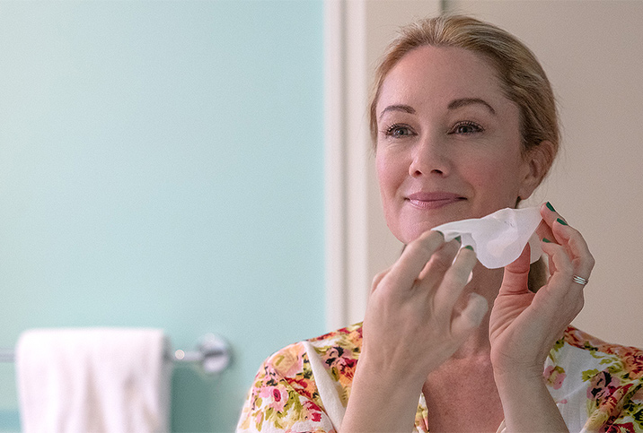 A woman holds a tissue to her face as she cleans it.