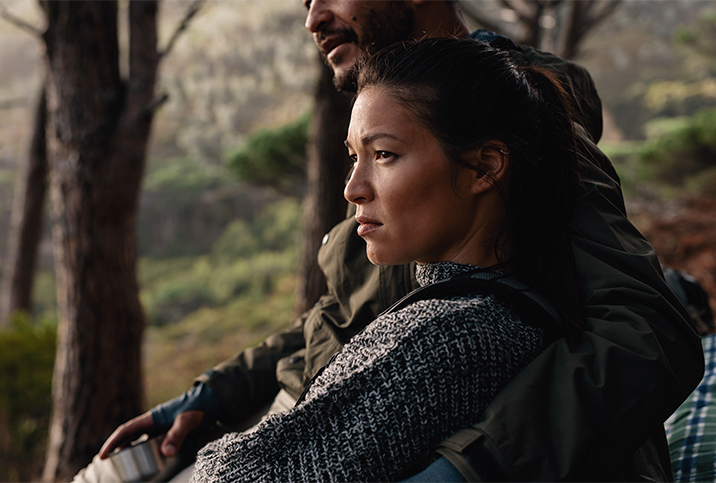 A couple sits together in the forest looking out towards the distance.