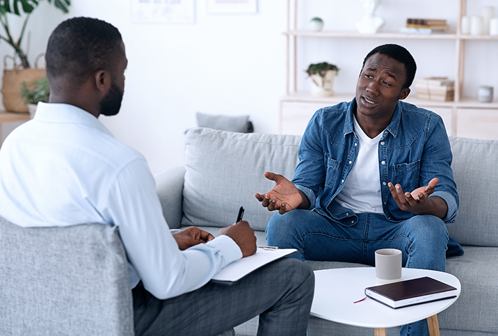 A man talks to his therapist with his arms shrugging and palms up.