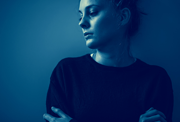 A woman looks down and to the side with a blue tint over the photo.