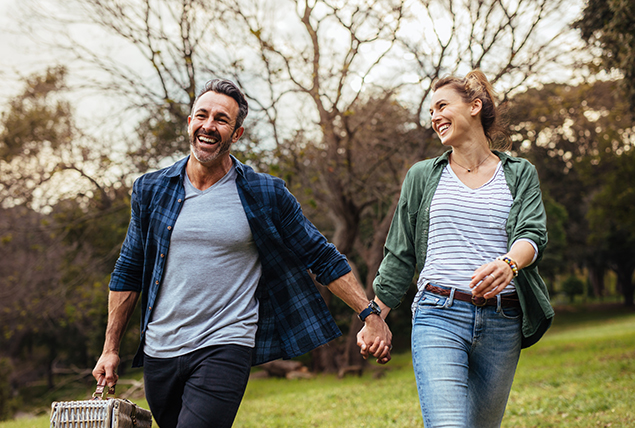 A man and woman walk through a field, smiling and holding hands.