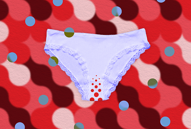 Lavender underwear with red dots in the crotch area lays against a red patterned background.