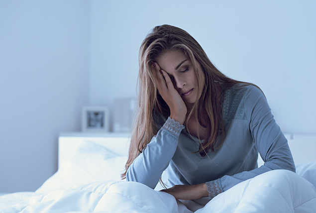 A tired woman sits in bed with her head resting in her hand.