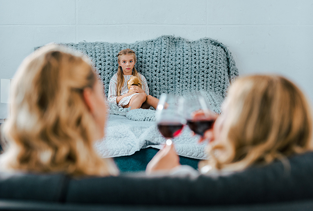 A child watches in the background as two women cheers their wine glasses.