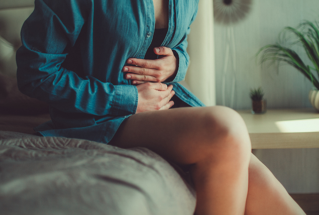 A woman sits on a sofa holding her stomach.