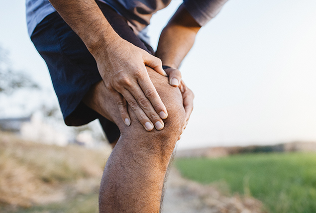 A man holds his right knee in pain and rubbing it.