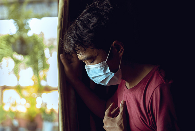 A man with a face mask holds onto the drapes as he pushes his other hand to his chest.