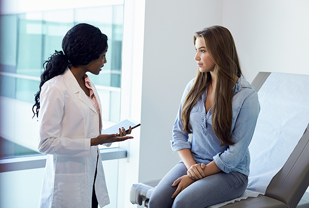 A woman sits on a hospital bed listening to a female doctor.