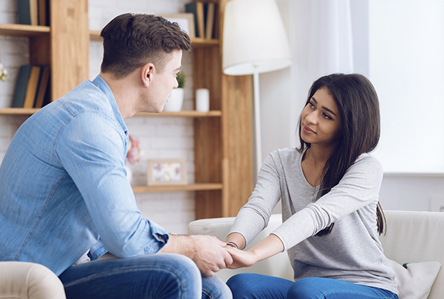 man and woman hold hands as they talk and sit on a couch