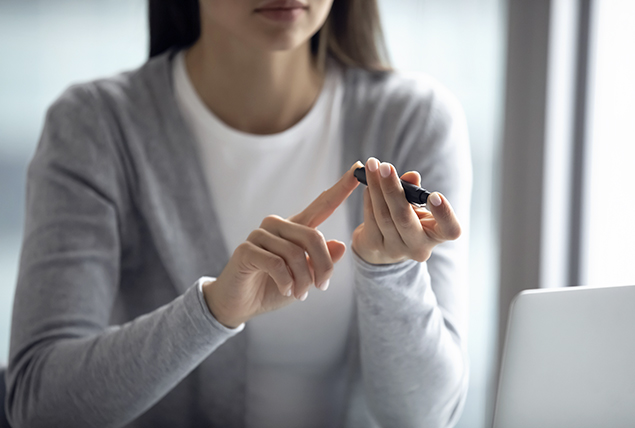 woman in gray cardigan checks her blood sugar on her finger tip