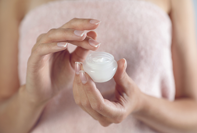 hands holding a jar of white lotion about to dip a finger in