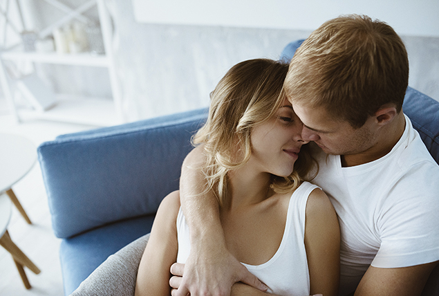 man and woman cuddle on blue couch about to kiss