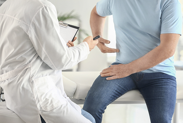 man in blue shirt points to his side as he talks to doctor and sits on doctors table