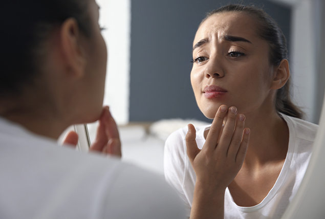 woman checks her complexion in mirror and looks concerned