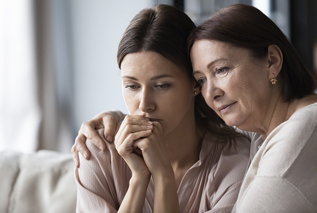 mother embraces daughter who holds her hands over he face in stress