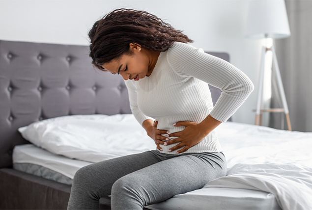 A woman holds her stomach as she sits on the bed.