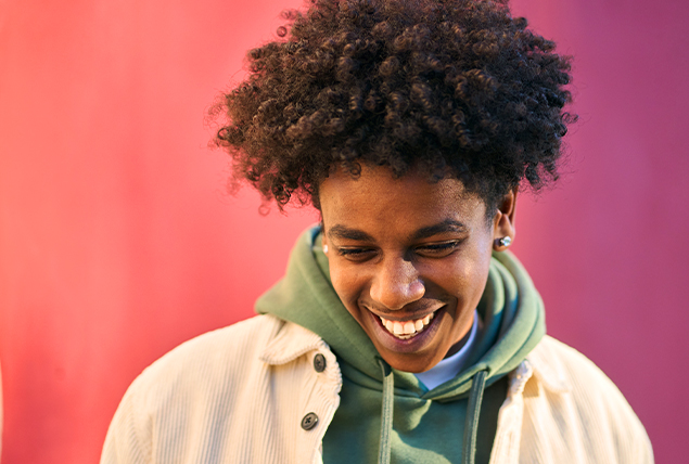 A man in casual clothing smiles as he looks down.