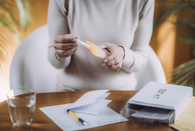 woman with beige sweater puts test tube in to padded envelope of test kit