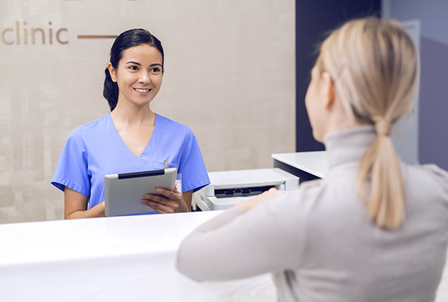 A woman approaches a counter with a nurse on the other side.