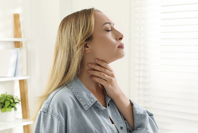 A woman holds her hand to her neck as she feels for her thyroid gland.