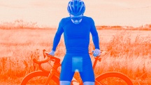 A blue man stands beside his orange bike looking down at his spontaneous erection.